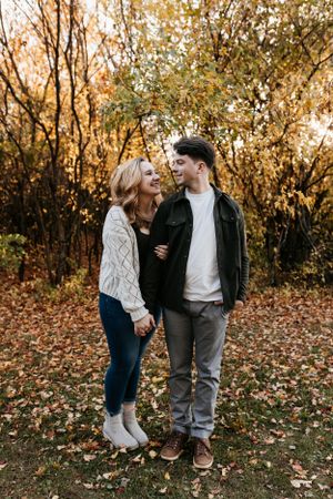 Couple in casual sweaters standing together among fall foliage.