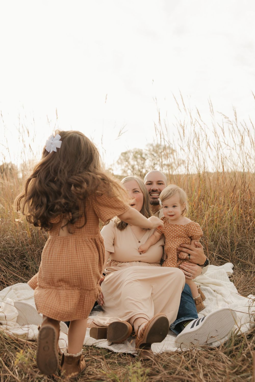 A family sits together in a golden field of tall grass during sunset, creating a warm and intimate moment.