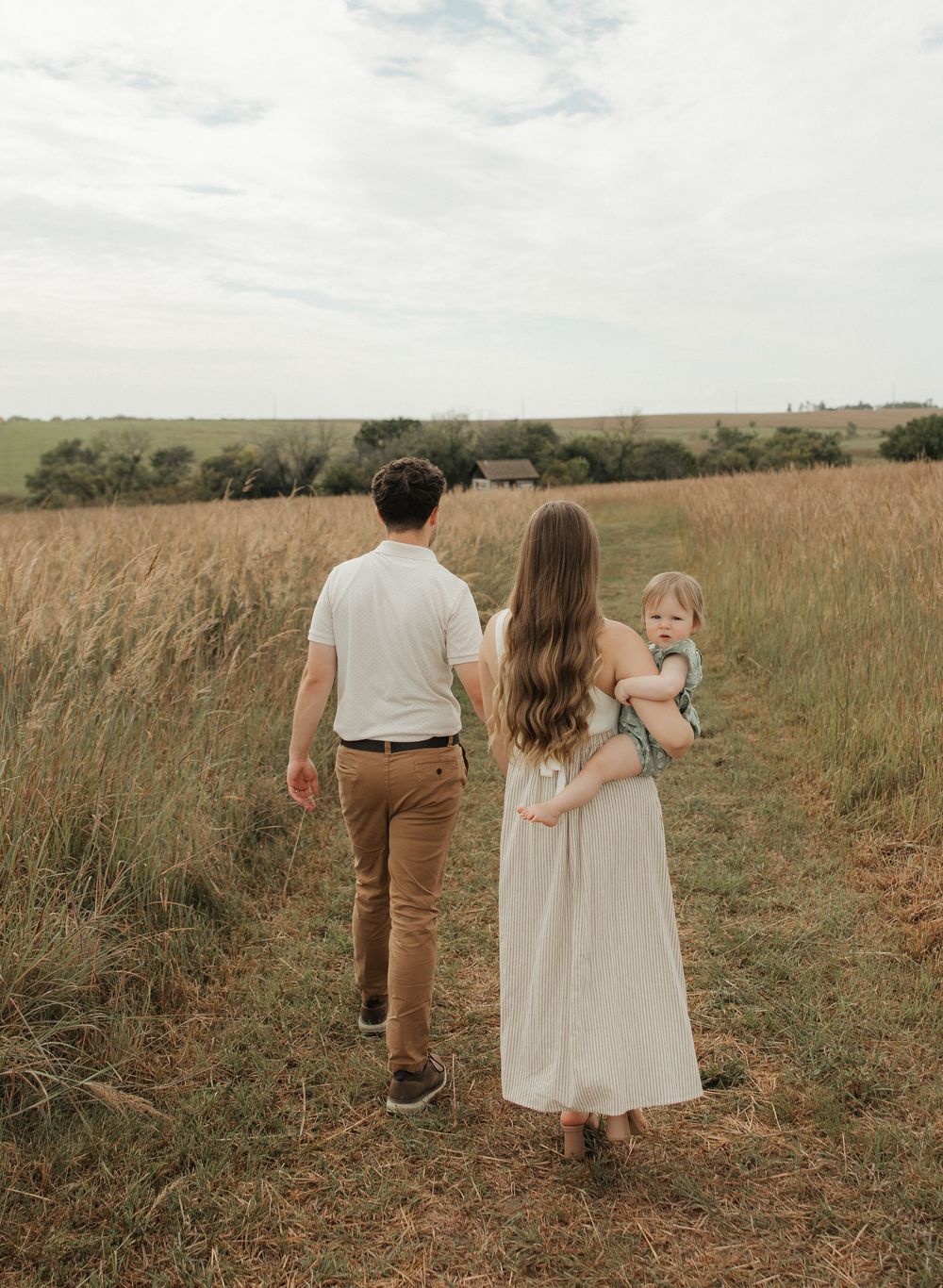 Couple walking through a golden wheat field at sunset holding hands in a romantic countryside setting.