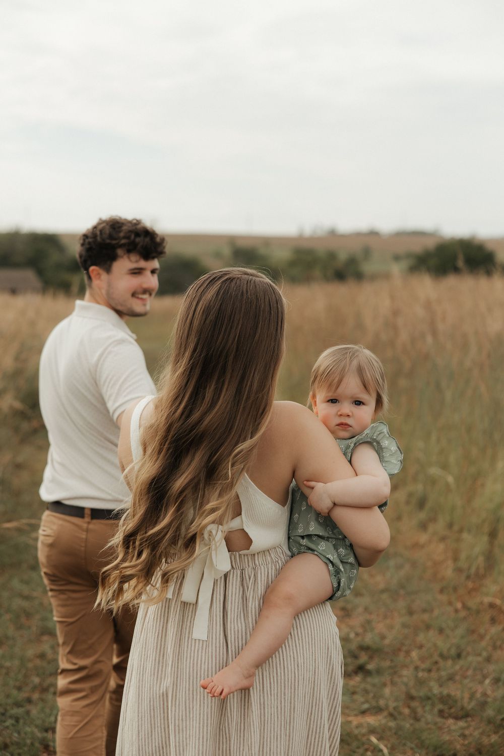 A family shares tender moments together while walking through a golden field at sunset.