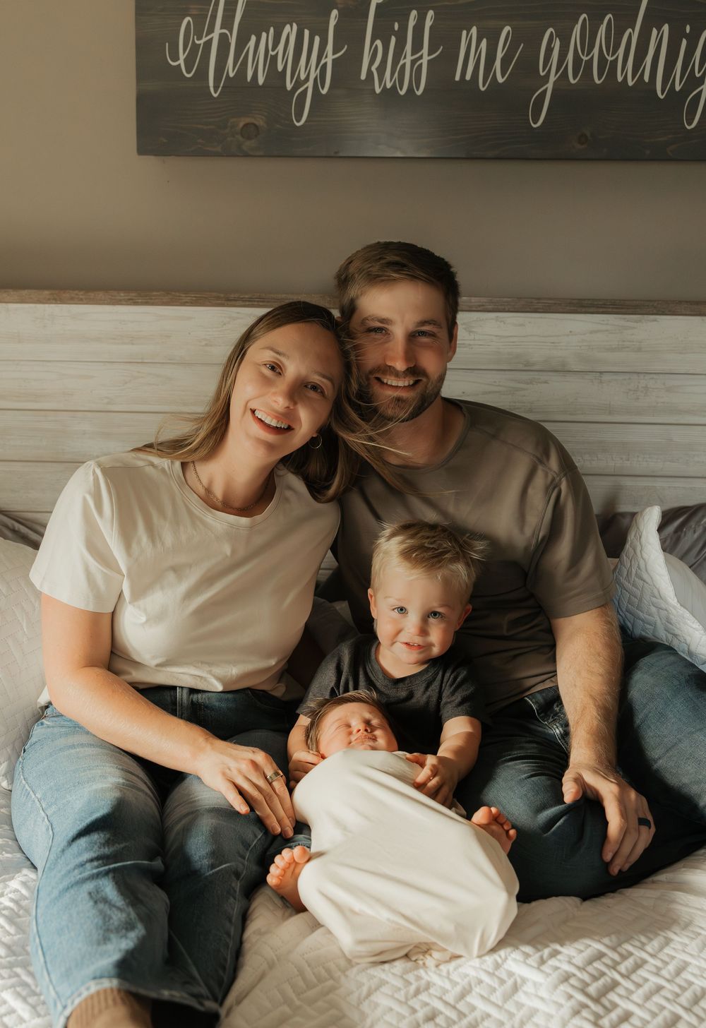 A family lounges together on a cozy white bed, sharing tender moments in matching white t-shirts and casual attire.