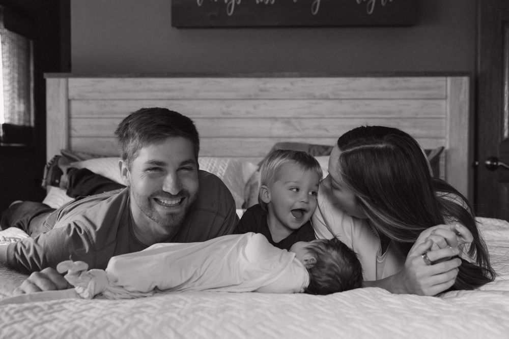 A family shares a joyful moment together while lying on a bed in black and white photography.