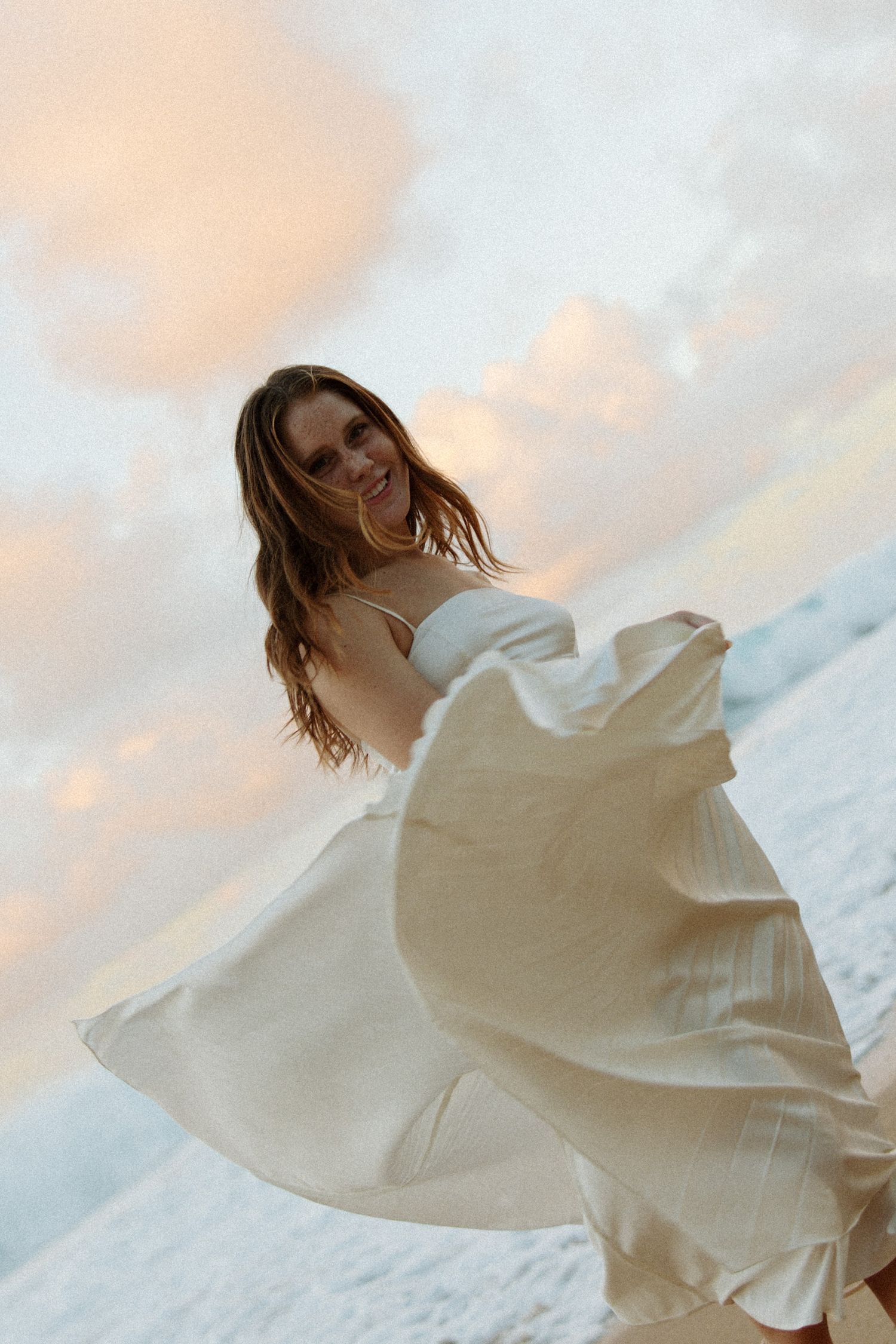 A woman in summer attire poses thoughtfully against a lush mountain backdrop.