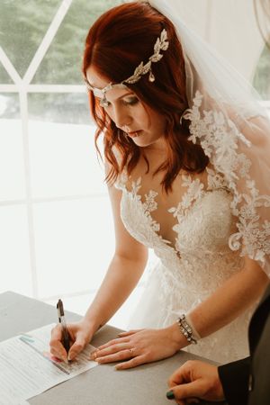 A bride in a lace wedding gown signs documents during a wedding ceremony.