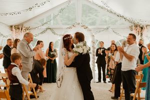 Wedding guests dance and celebrate beneath a white tent during a reception.