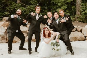 Wedding party poses playfully on rocks in an outdoor setting.