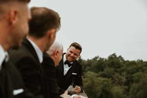 Groomsmen sharing laughs during outdoor wedding ceremony.