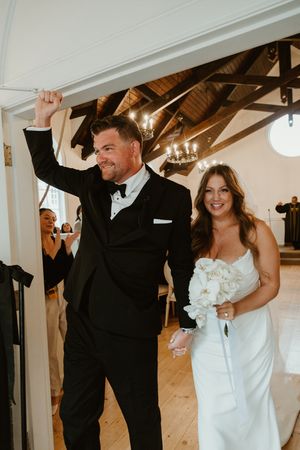 Newlyweds sharing a playful dance moment under rustic wooden beams and chandeliers.