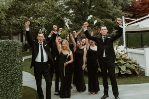Wedding party throws their hands up in celebration on outdoor garden pathway.