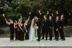 Wedding party poses for formal group photos on outdoor stone pathway surrounded by greenery.