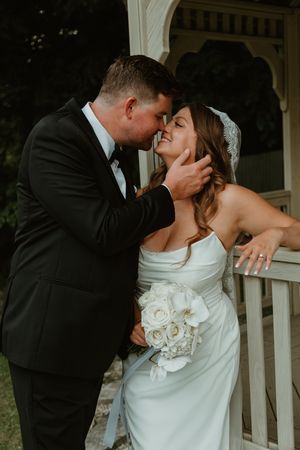 Romantic moment between newlyweds on white wooden porch during wedding photoshoot.