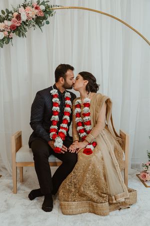 Traditional Indian wedding couple sharing intimate moment under floral arch.