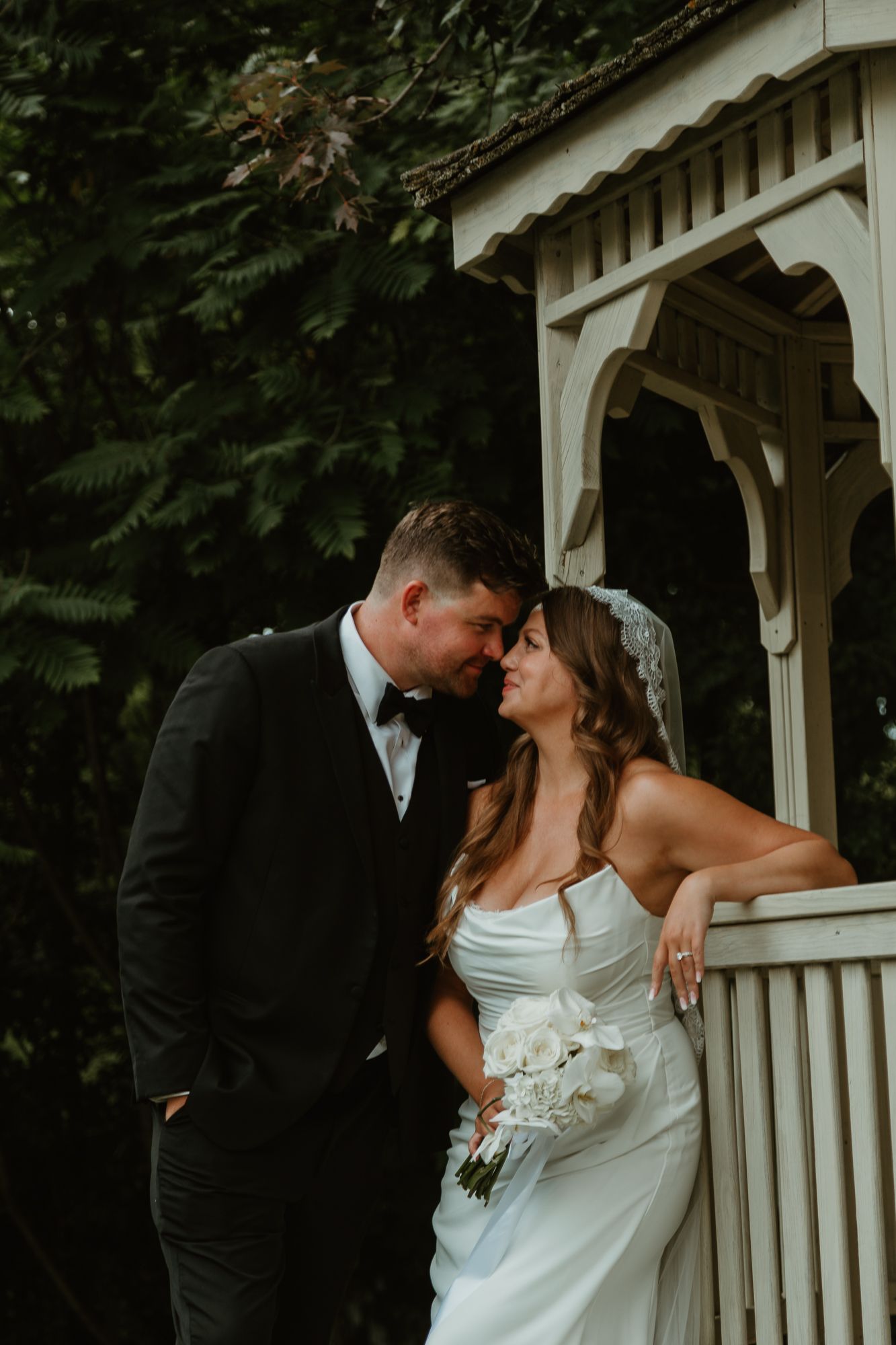 Intimate wedding portrait session on a white gazebo surrounded by lush greenery.