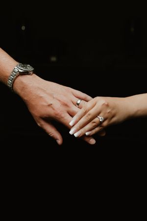 Close-up shot of hands displaying engagement rings against a dark background.
