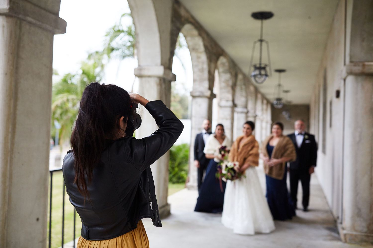 A photographer captures a wedding ceremony under arched columns of a building.