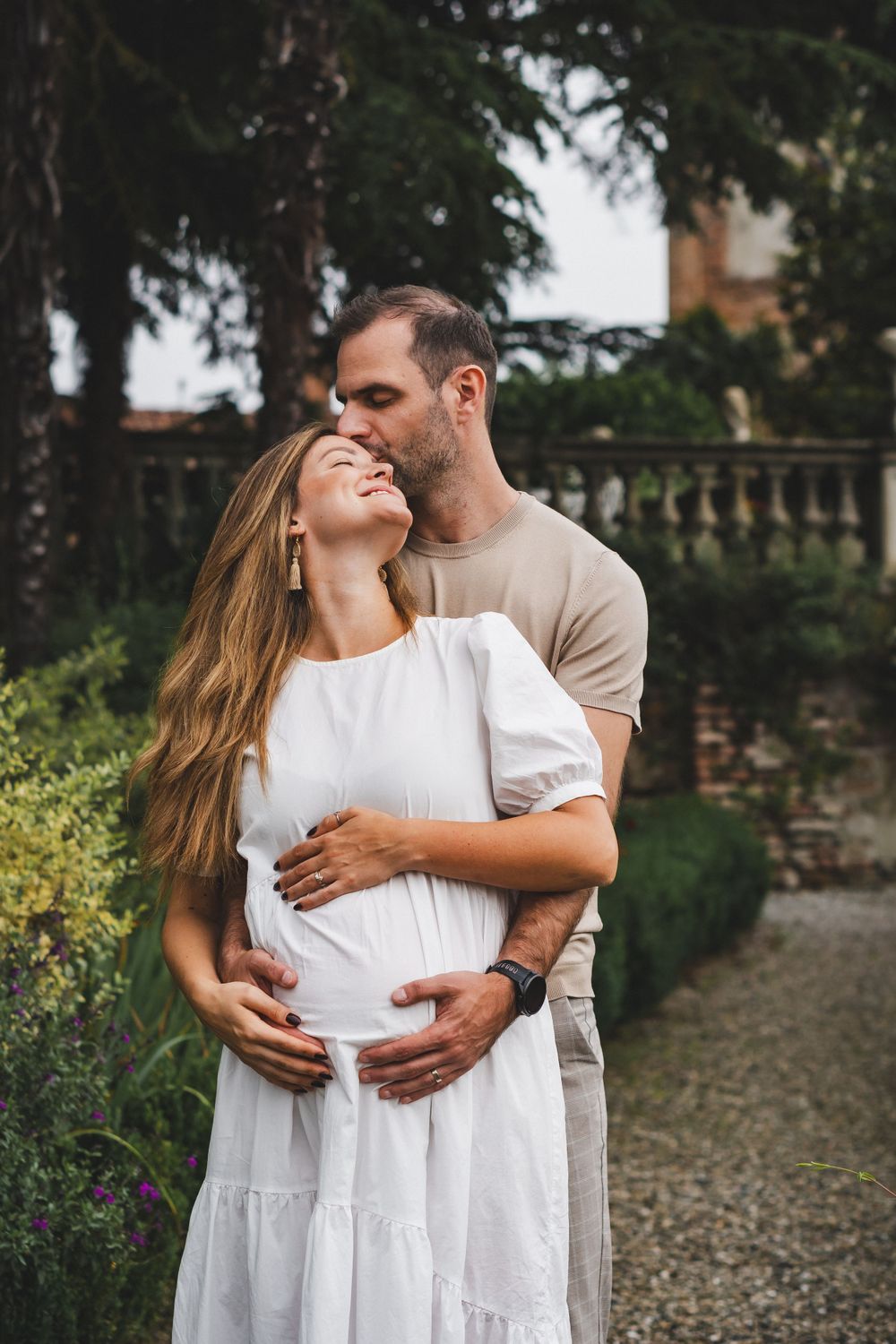 Romantic couple embracing in a garden setting with stone architecture in the background.