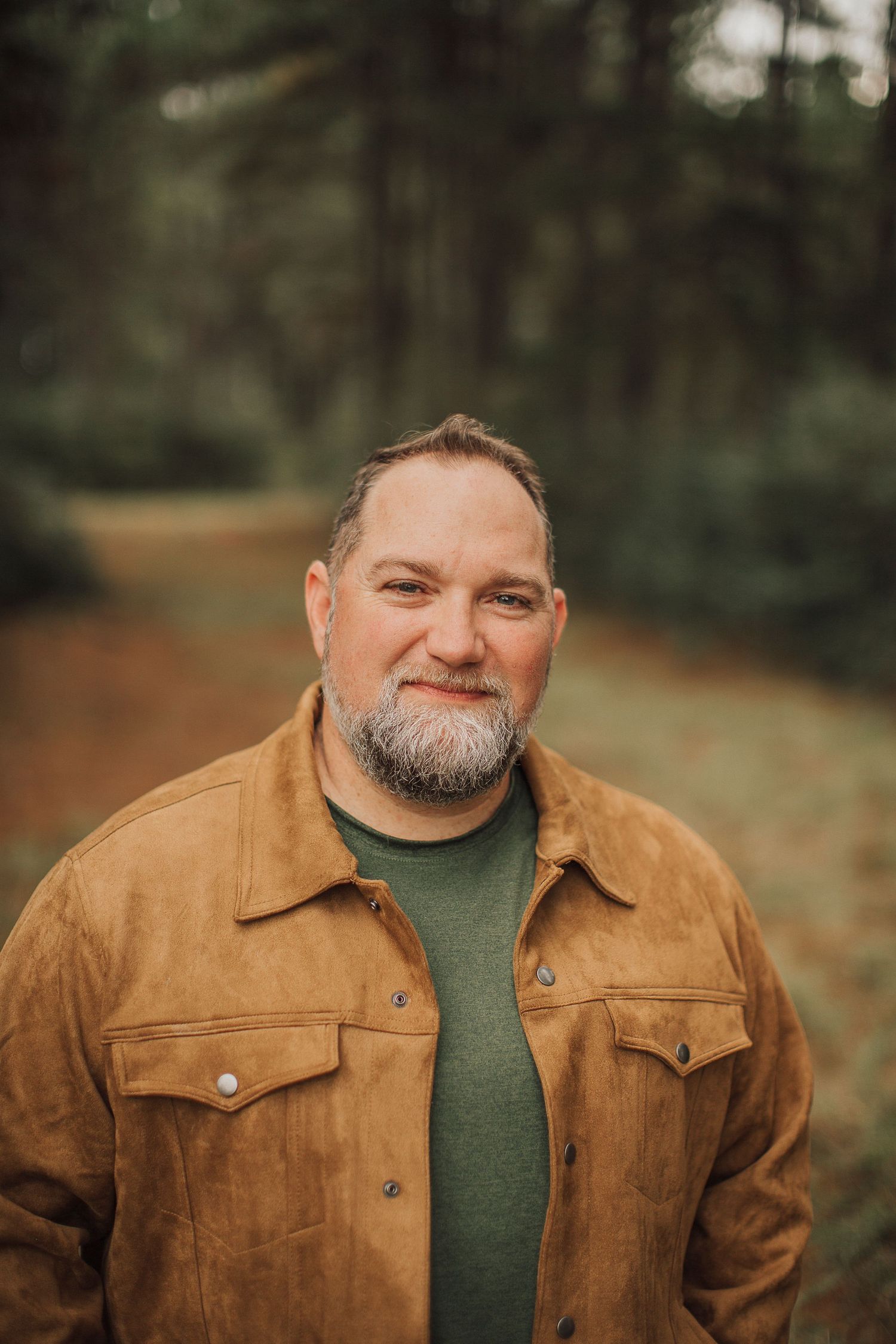 Portrait of person wearing brown suede jacket and green shirt in outdoor setting.
