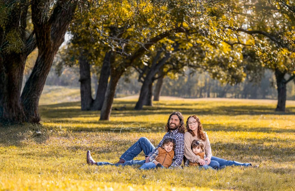 A family relaxes together on a blanket under golden autumn trees in a sunlit park.