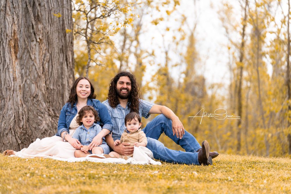 A family sits together on a blanket under autumn trees in a park on a golden afternoon.