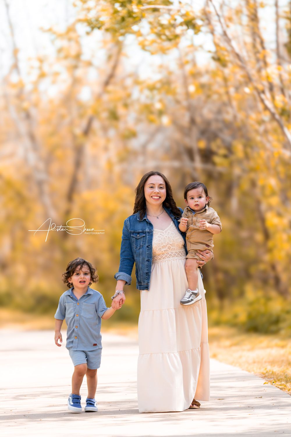 Family walks together on path surrounded by golden autumn foliage with warm sunlit afternoon lighting.