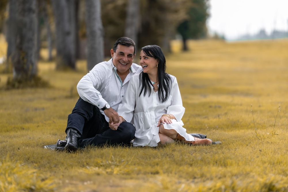 A couple in white outfits lies together on a grassy hillside during a romantic outdoor photoshoot.
