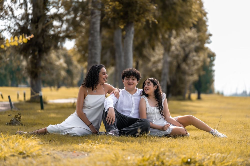 Family relaxing together on a grassy field during a sunny autumn day with golden yellow foliage in the background.