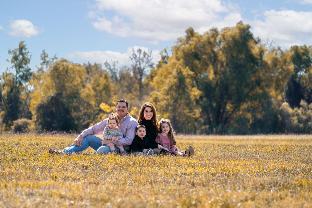 Family enjoying a sunny autumn day lying in a field of yellow wildflowers with trees in the background.