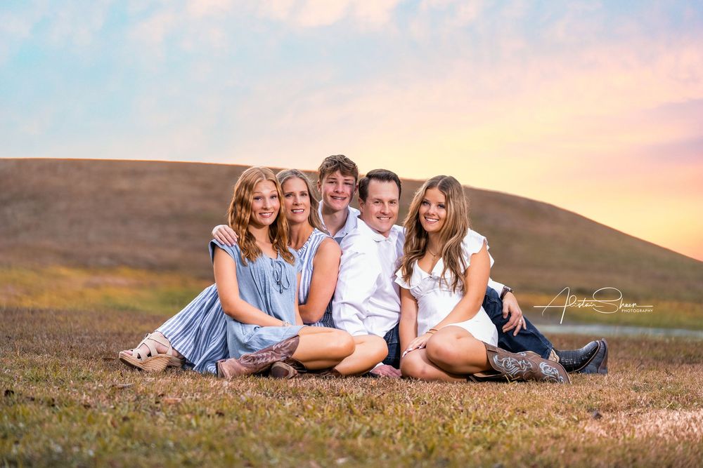 Family group poses together on grassy hillside during golden sunset photo session.