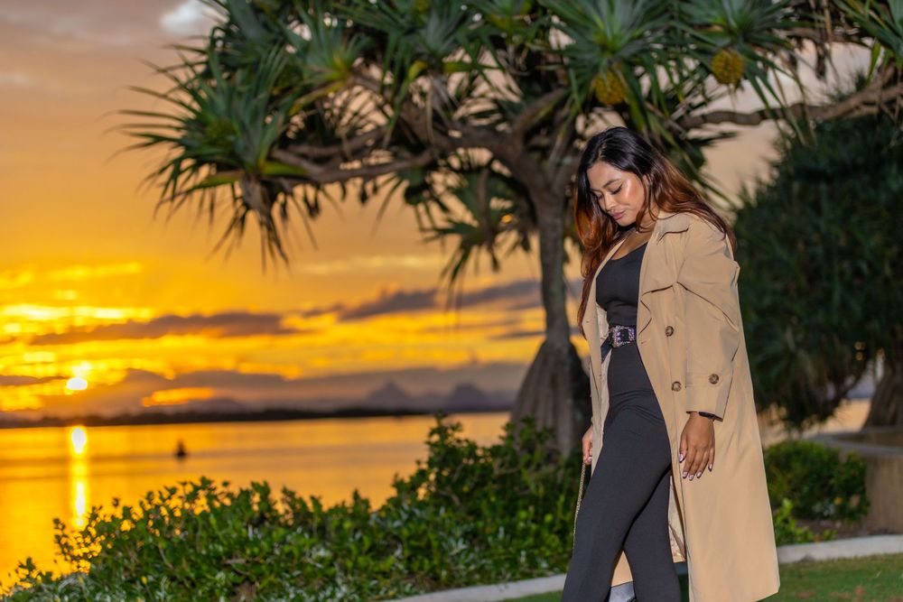 Fashion shoot featuring trenchcoat outfit against dramatic orange sunset by the water.
