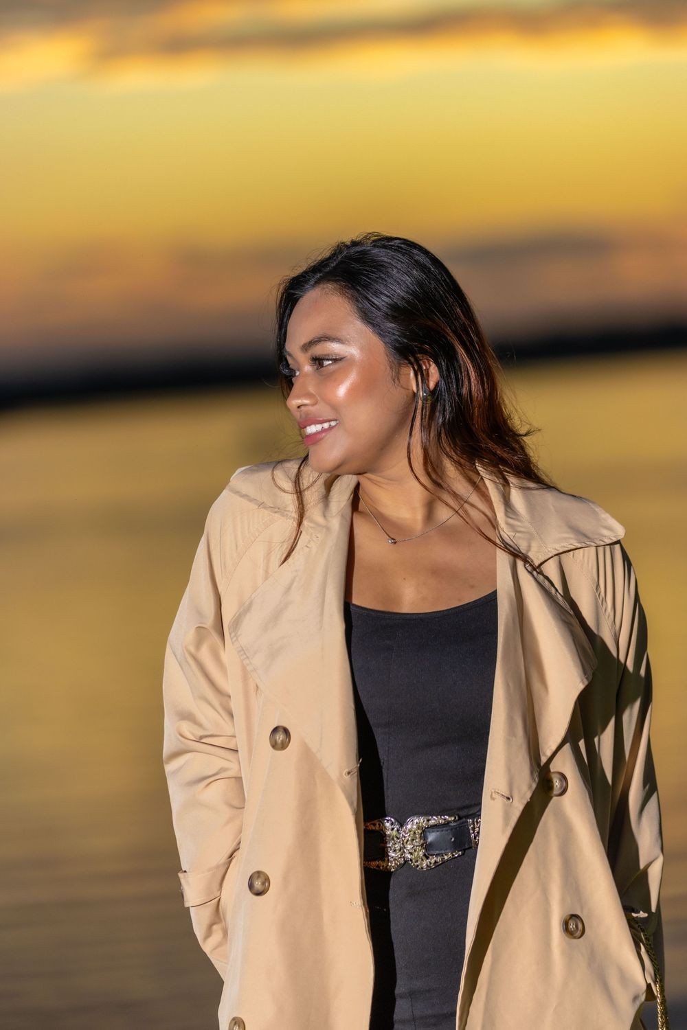 A gorgeous sunset provides warm golden lighting as someone poses in a stylish beige trenchcoat.