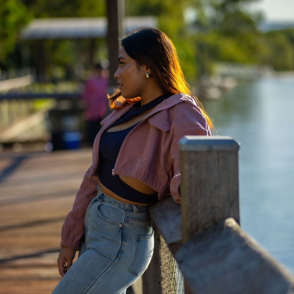 Casual outfit with pink jacket and jeans while posing on waterfront boardwalk during sunset.
