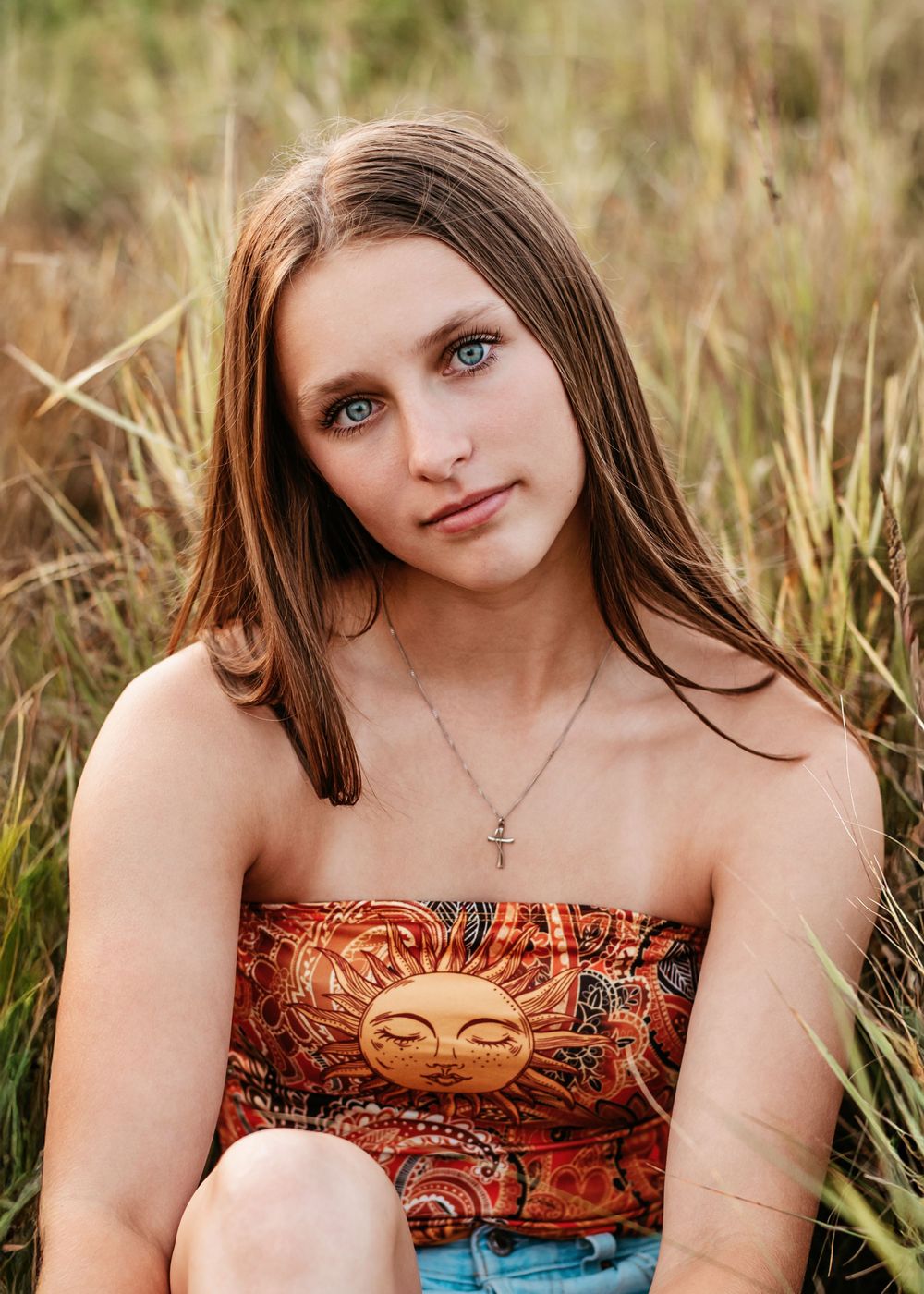 A person in an orange patterned strapless dress poses outdoors in tall grass during golden hour lighting.