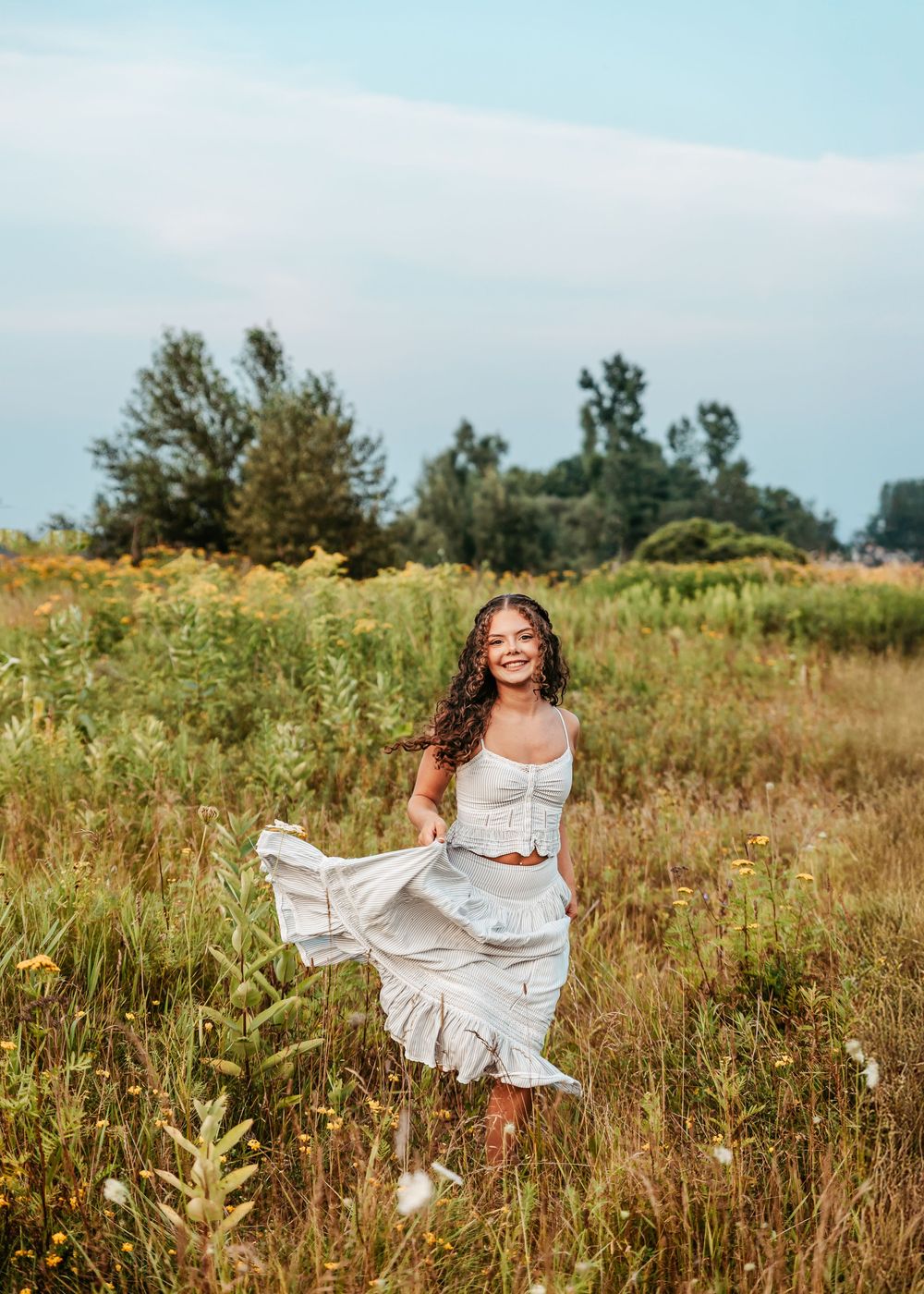 A person in a flowing white dress twirls gracefully through a golden wildflower meadow on a sunny summer day.