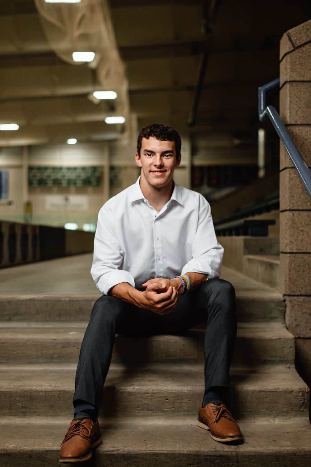 Person in white dress shirt and dark pants sits casually on concrete steps in a parking structure.