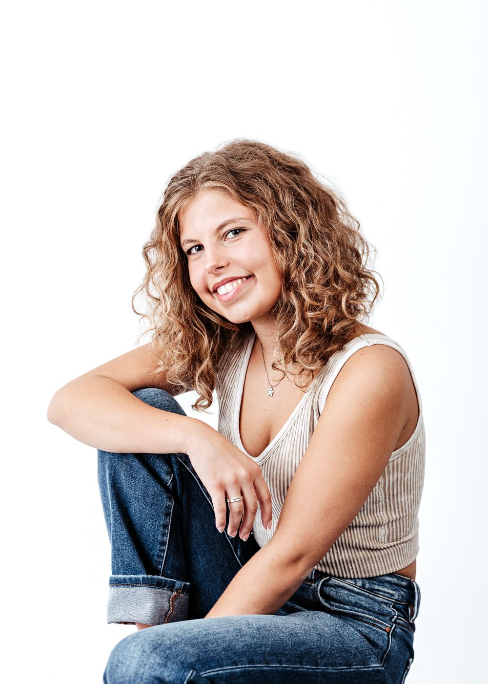Person in white tank top and jeans poses casually in a series of four relaxed studio portraits.
