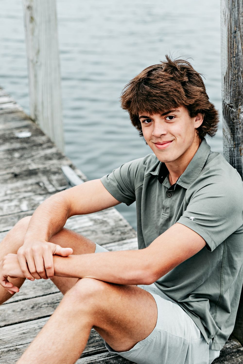 A casual portrait series on a wooden dock by the water showing someone wearing a grey polo shirt.