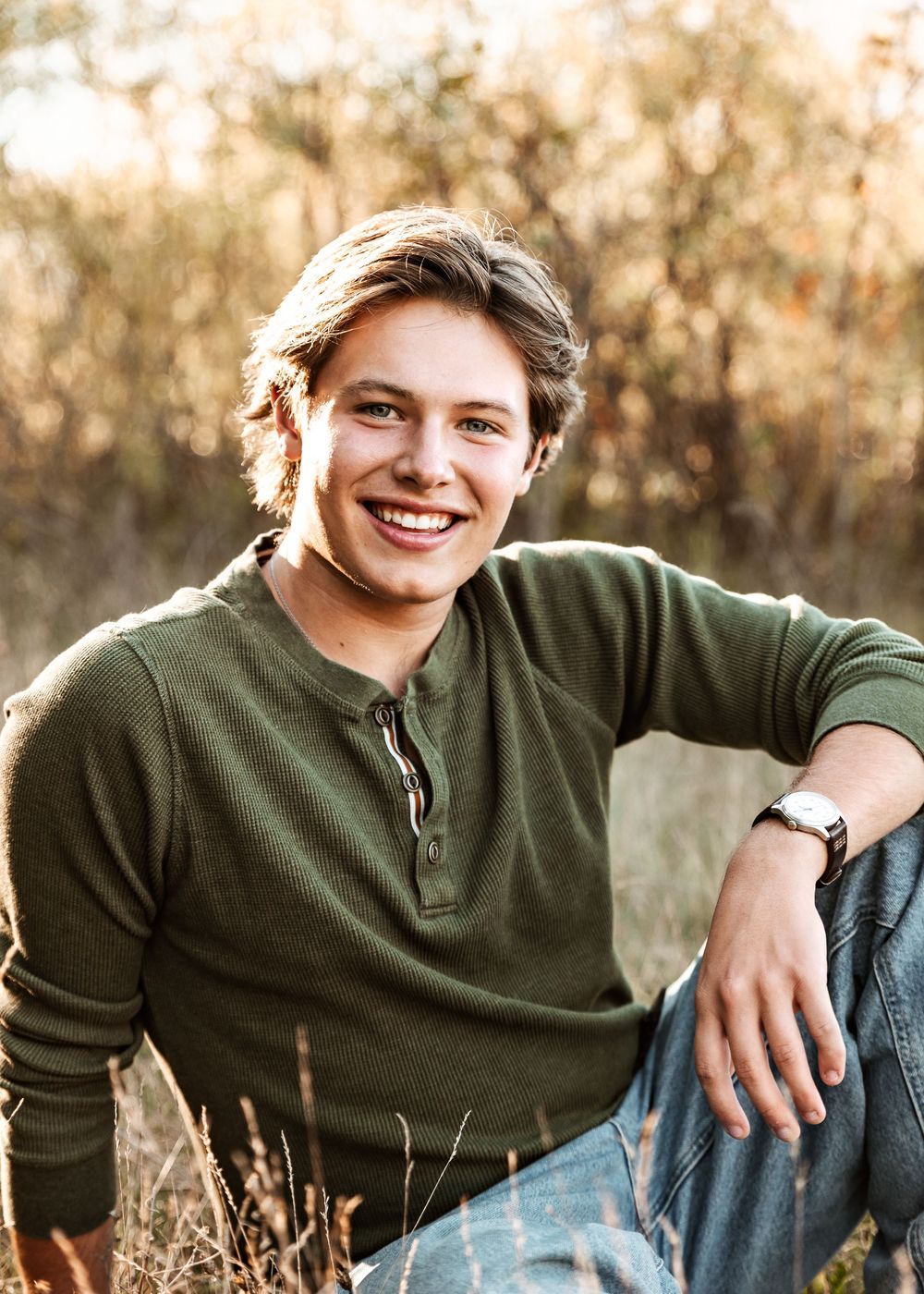 Casual outdoor portrait in autumn field with green henley shirt and denim against natural brown foliage background.
