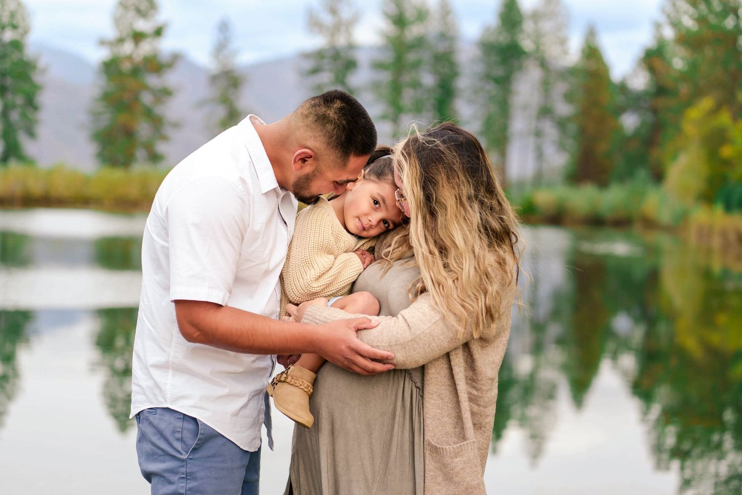 portrait of a family of 3 as they snuggle by a pond with mountain views
