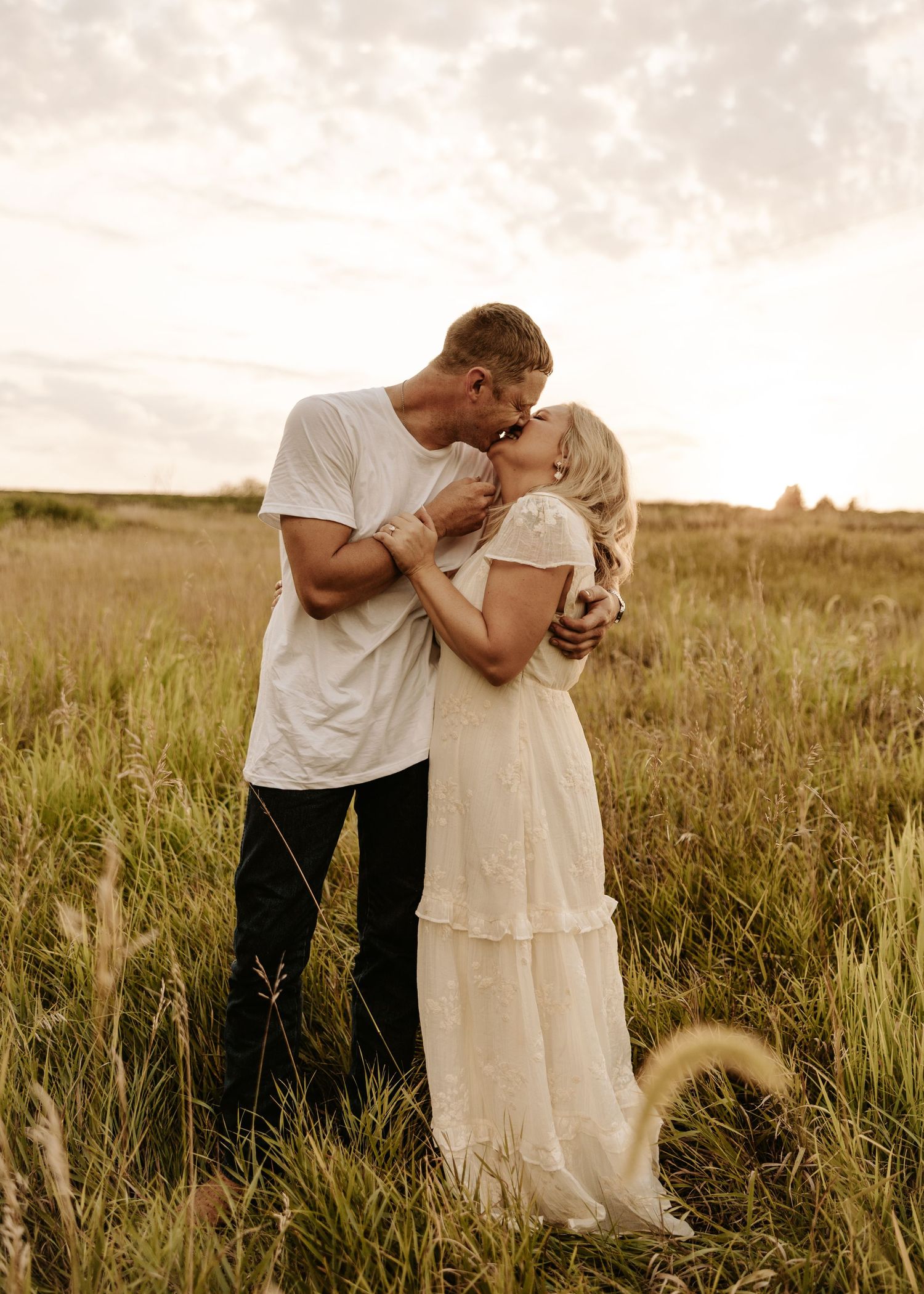 A couple stands against a rustic brick wall with boarded windows and climbing vines at sunset.