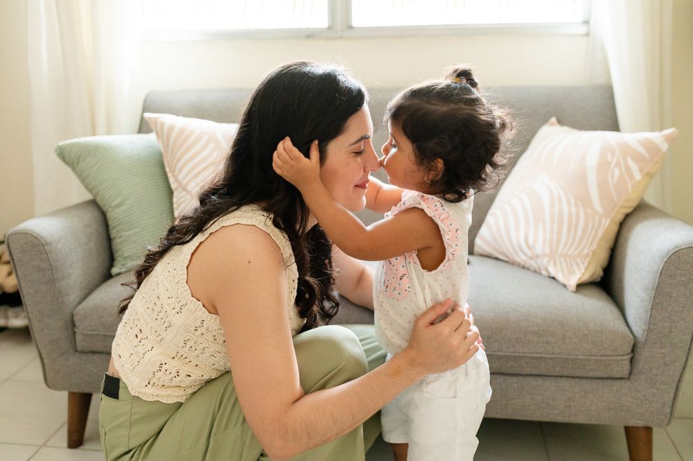Tender moment shared between parent and child on a grey couch in a bright living room.