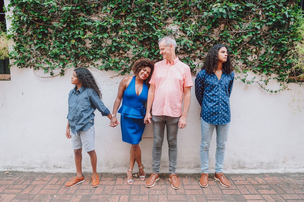 Group posing casually against white wall with green vine backdrop.