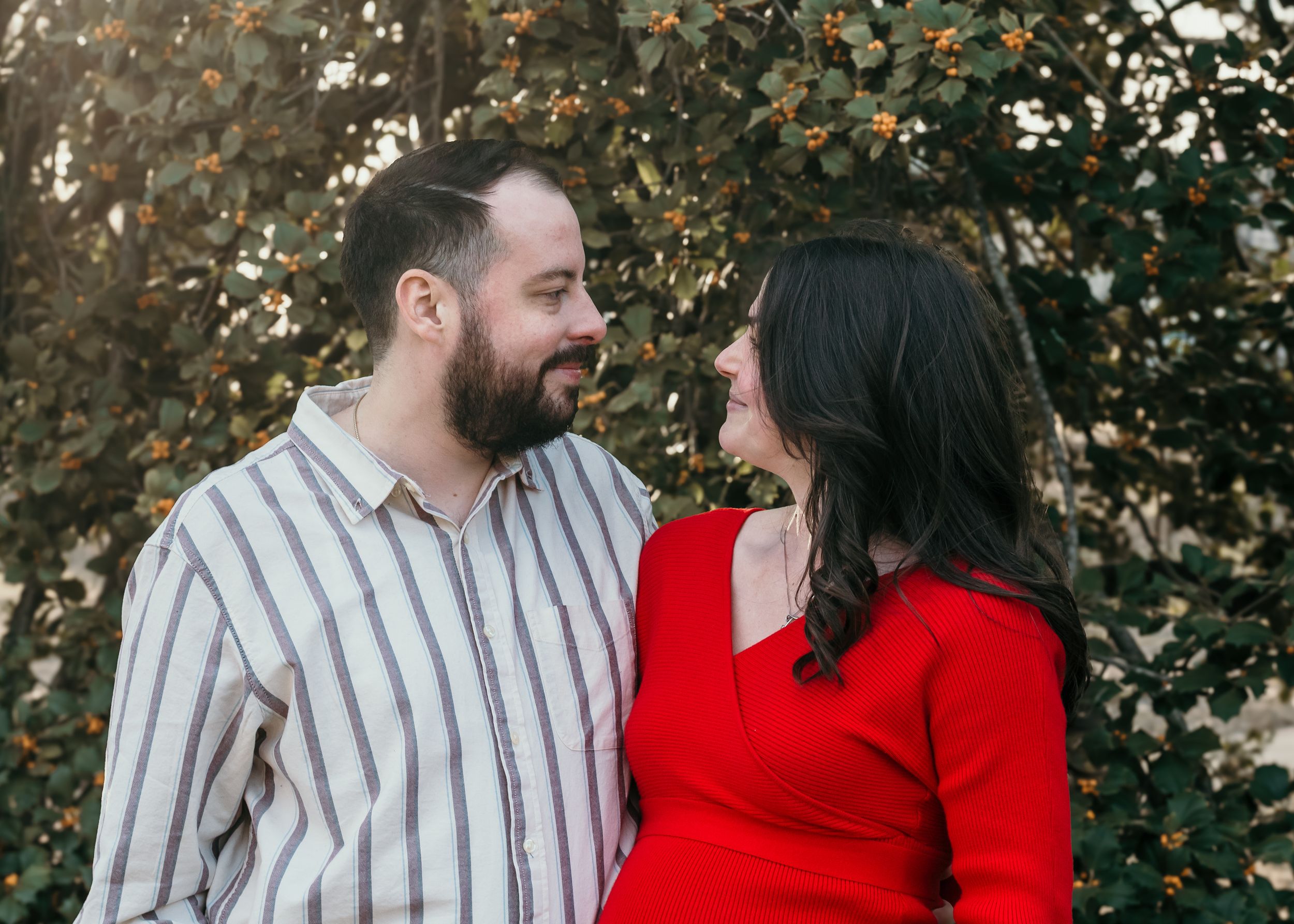 A couple embrace outdoors during an autumn maternity photoshoot.