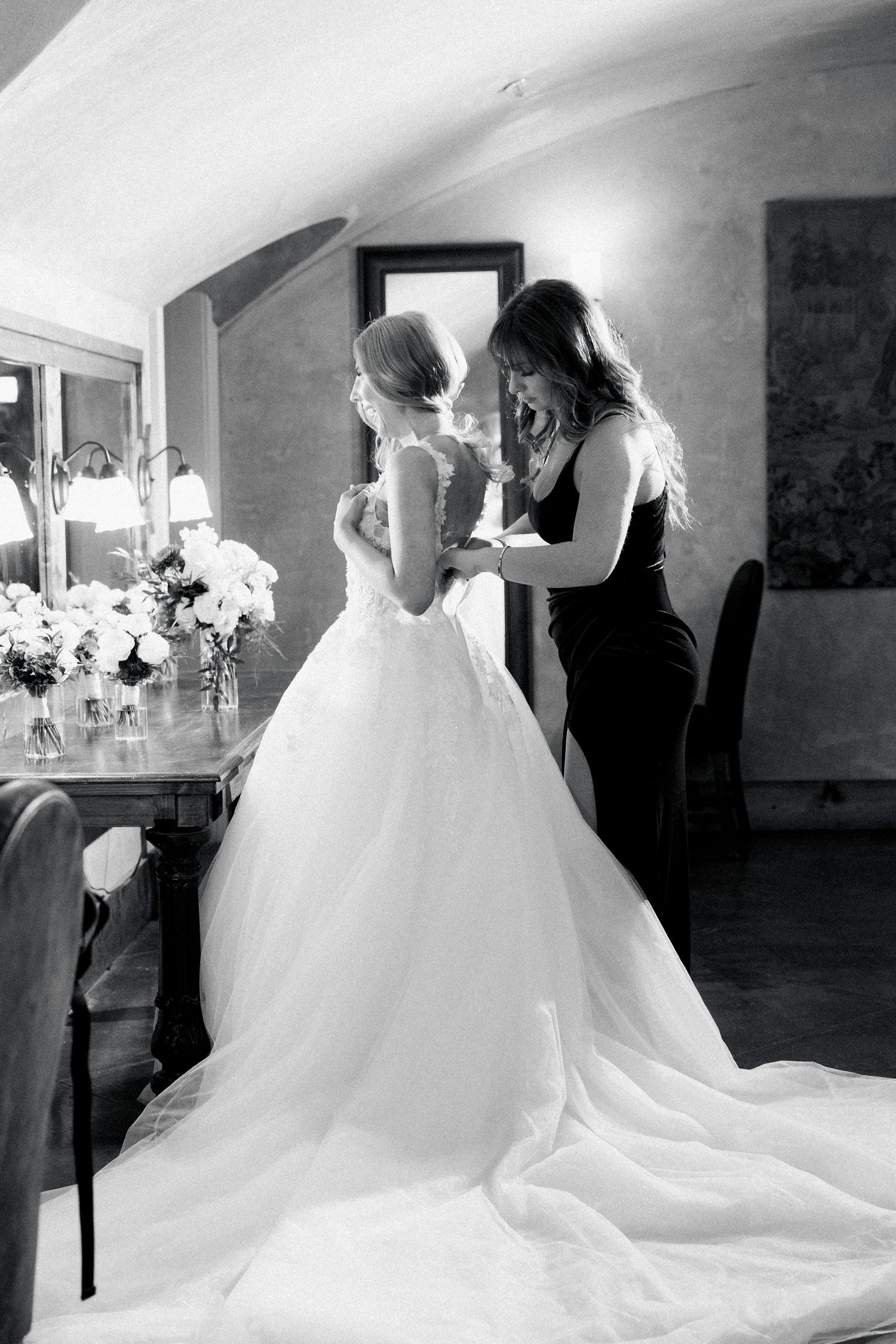 Black and white photo of a bridesmaid helping a bride with her elegant ball gown wedding dress before the ceremony at montaluce winery.