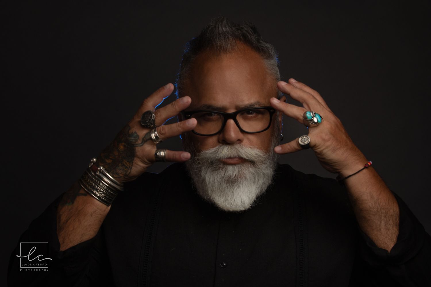 Professional headshot of someone with a white beard, light blue shirt and clear glasses against dark background.