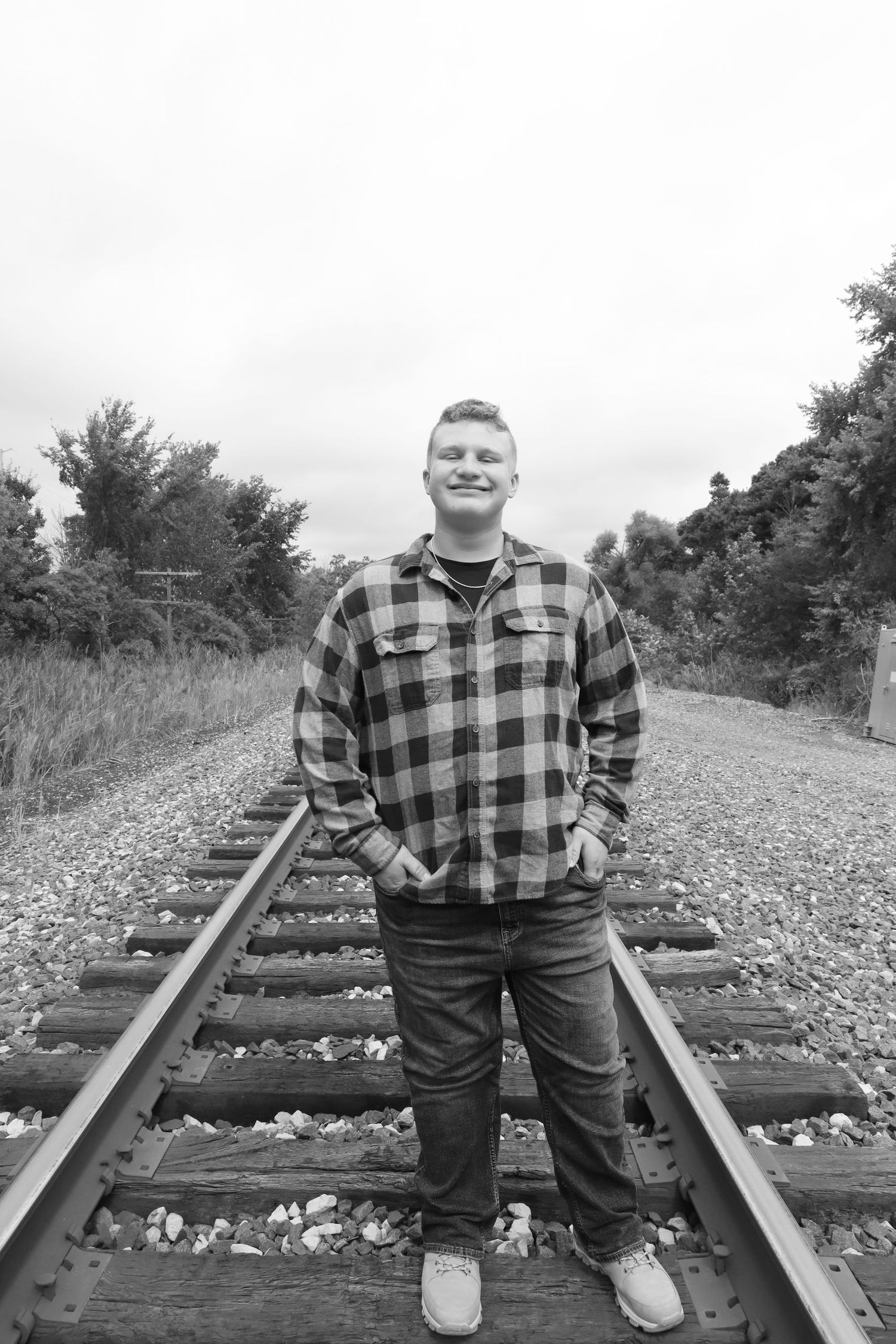Person in plaid flannel shirt stands on railroad tracks in black and white photo.