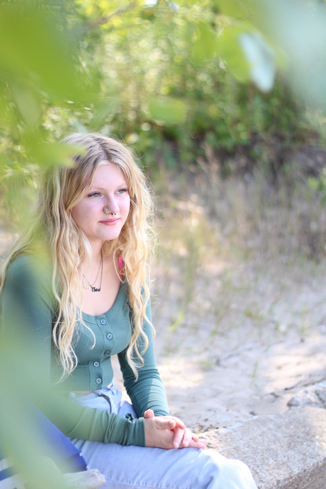 A person in a green top sits outdoors against a blurred natural background in soft lighting.