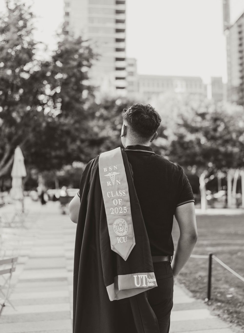 Graduate wearing a class of 2020 graduation sash and cap viewed from behind on an urban campus.