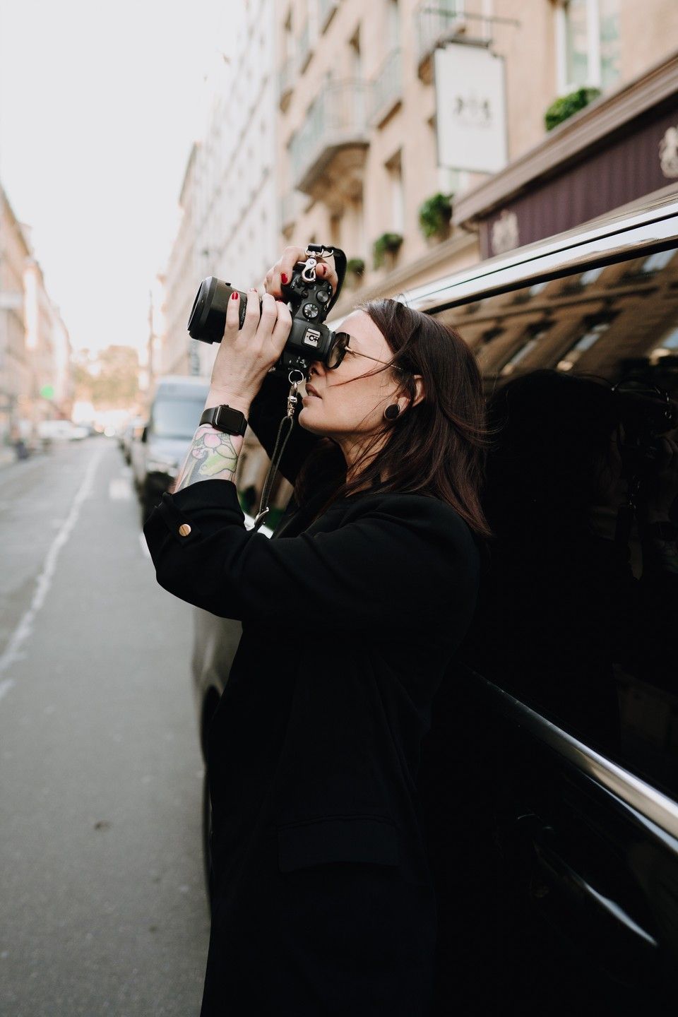 Photographer in black clothing holds up a camera to take a picture on a European city street with classic buildings.