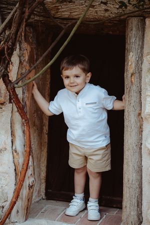 Child exploring wooden structure while wearing white polo and khaki shorts.