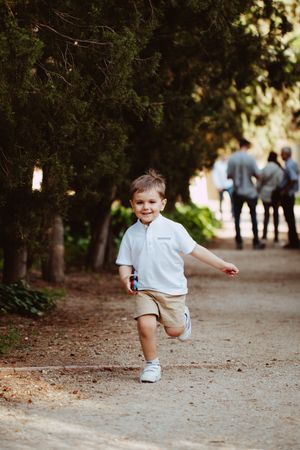 Child running playfully on a dirt path surrounded by trees.
